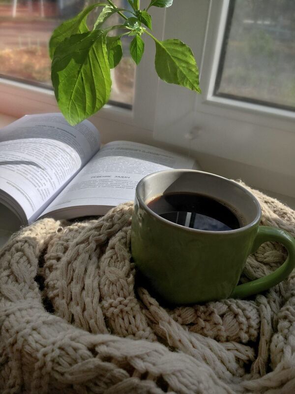 چائے کا کپ، کتاب اور سبز پتوں کے ساتھ لکڑی کی میز پر رکھا ہوا آرام دہ منظر